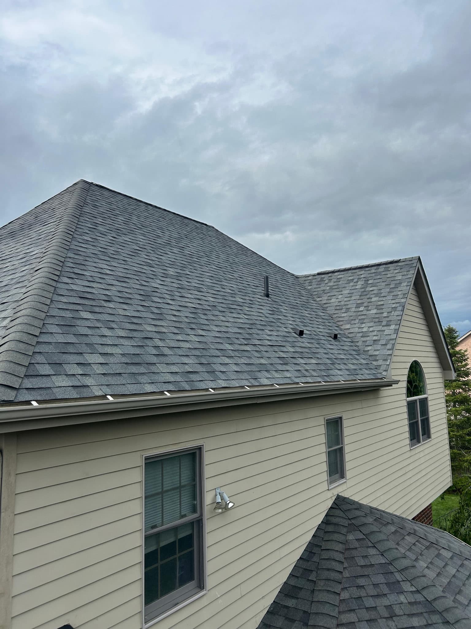 Wide view of a freshly installed architectural shingle roof on a tan-sided home